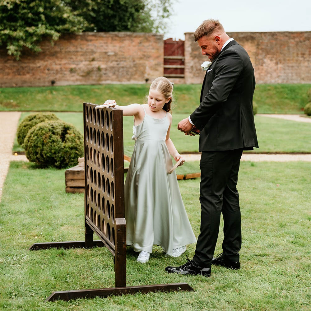 Giant Connect 4: Oversized wooden Connect 4 game standing on a garden patio for wedding guest entertainment.